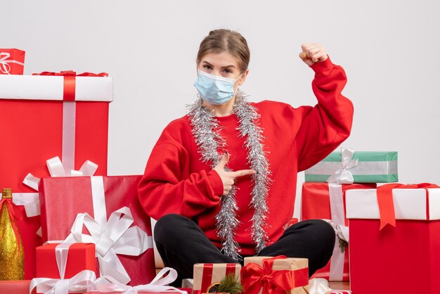 Front view young female sitting around christmas presents in sterile mask