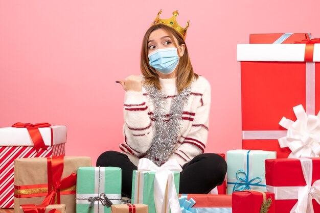 Front view young female sitting around christmas presents in sterile mask