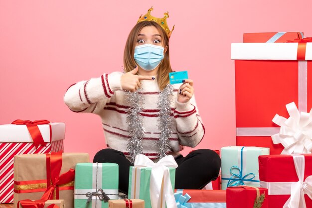 Вид спереди молодая женщина, сидящая вокруг рождественских подарков с банковской картой