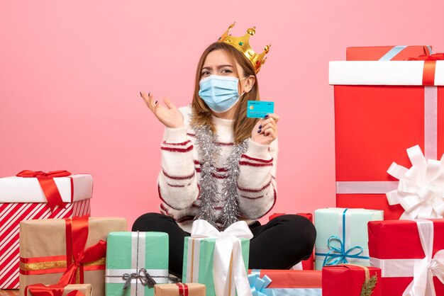 Front view young female sitting around christmas presents with bank card