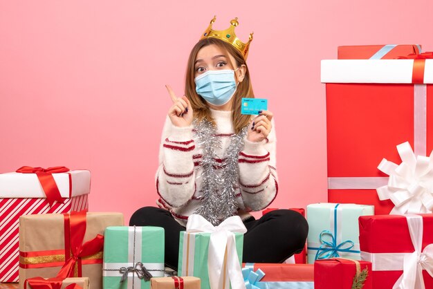 Front view young female sitting around christmas presents with bank card