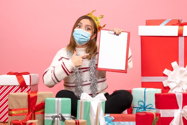 Front view young female sitting around christmas presents with file note