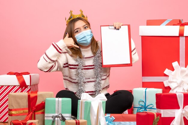 Front view young female sitting around christmas presents with file note