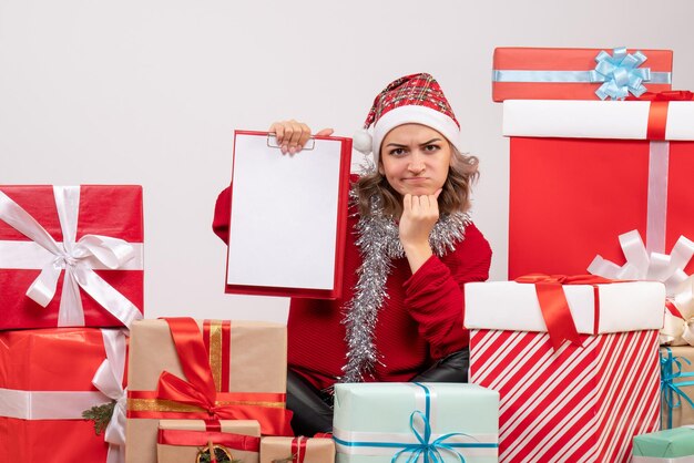 Front view young female sitting around christmas presents with note