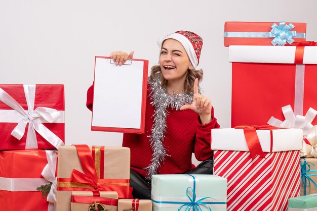 Front view young female sitting around christmas presents with note