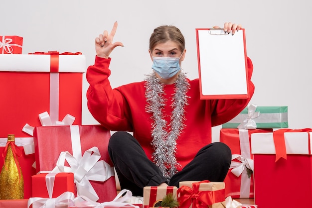 Front view young female sitting around christmas presents with note