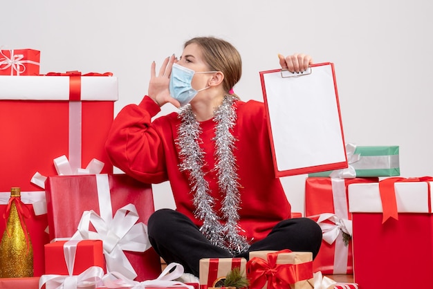 Front view young female sitting around christmas presents with note