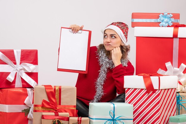 Front view young female sitting around christmas presents with note