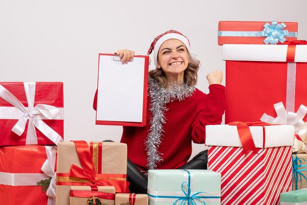 Front view young female sitting around christmas presents with note