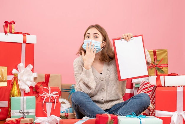 Front view young female sitting around xmas presents in mask with note