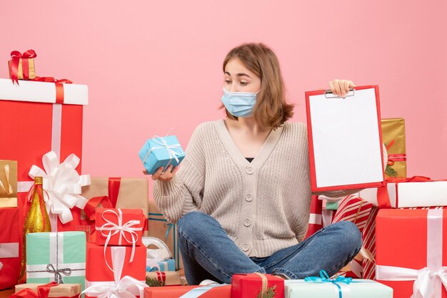 Front view young female sitting around xmas presents in mask with note