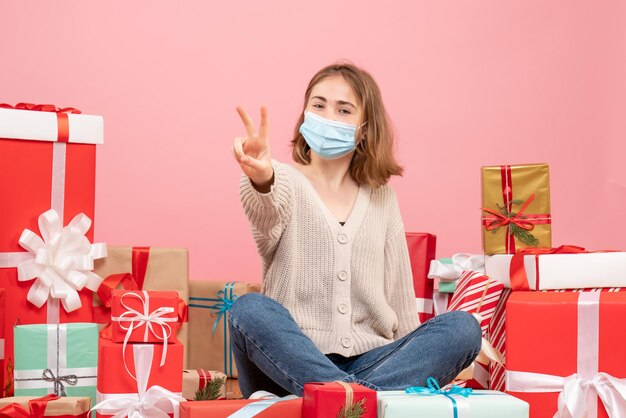 Вид спереди молодая женщина, сидящая вокруг рождественских подарков в маске
