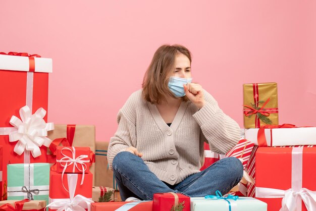 Вид спереди молодая женщина, сидящая вокруг рождественских подарков в стерильной маске