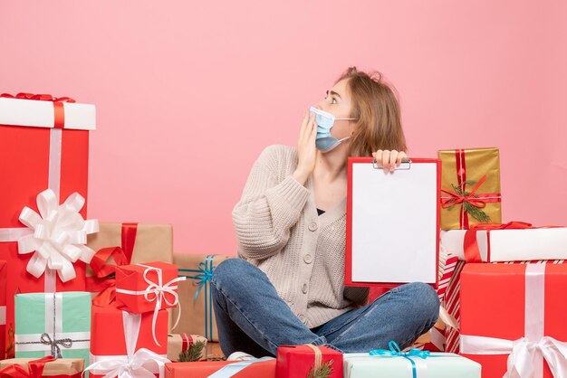 Вид спереди молодая женщина, сидящая вокруг рождественских подарков в стерильной маске