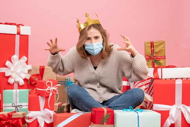 無菌マスクでクリスマスプレゼントの周りに座っている正面図若い女性