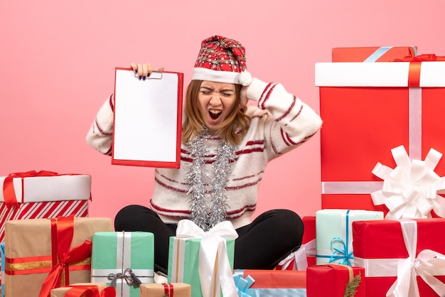 Бесплатное фото Вид спереди молодая женщина, сидящая вокруг рождественских подарков с файловой заметкой