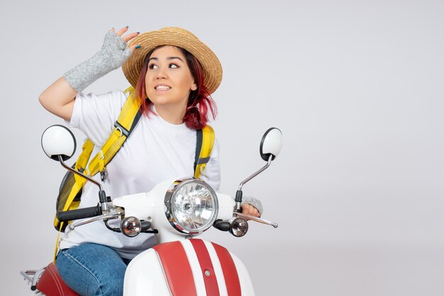 Front view young female sitting on motorcycle with backpack and hat on white wall