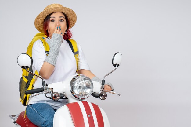 Front view young female sitting on motorcycle with backpack and hat white wall