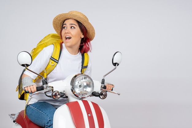 Front view young female sitting on motorcycle with backpack and hat white wall 