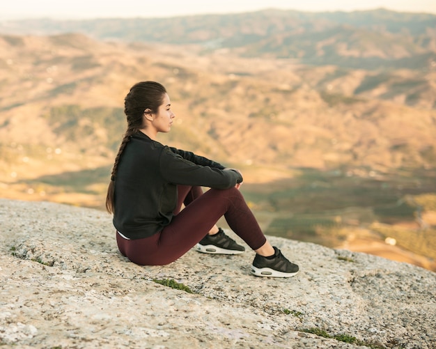 Front view young female sitting on top of mountain