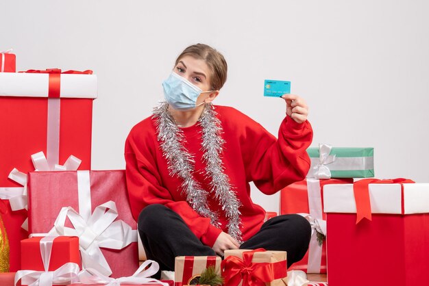 Front view young female sitting with christmas presents holding bank card