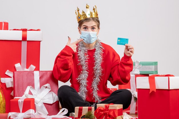 Front view young female sitting with christmas presents holding bank card