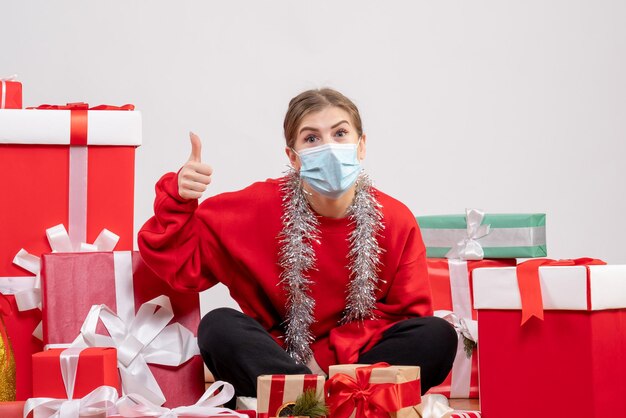 Front view young female sitting with christmas presents in mask