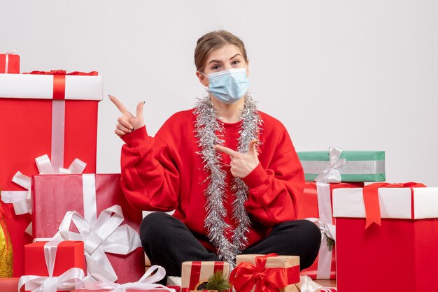 Front view young female sitting with christmas presents in sterile mask