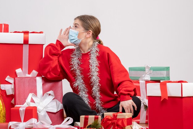 Front view young female sitting with christmas presents in sterile mask