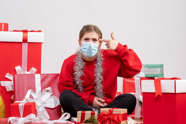 Front view young female sitting with christmas presents in sterile mask