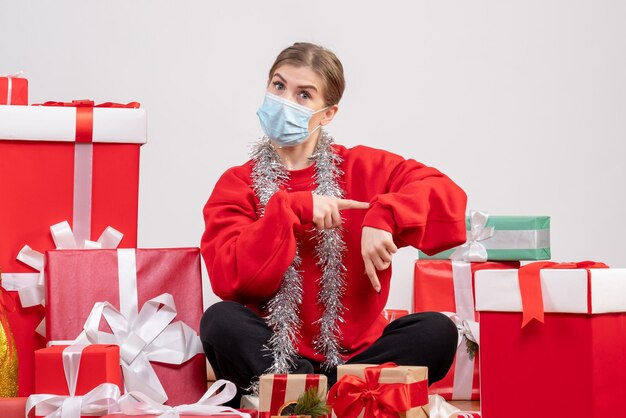 Front view young female sitting with christmas presents in sterile mask