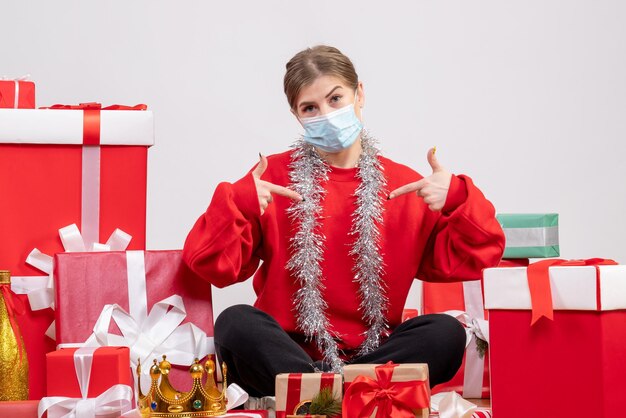 Front view young female sitting with christmas presents in sterile mask