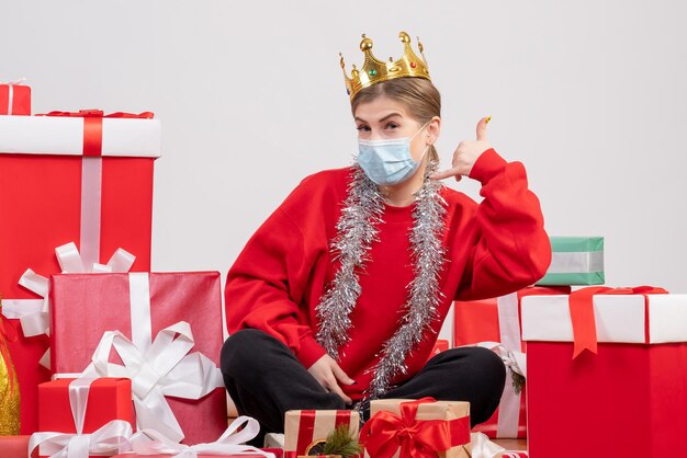 Front view young female sitting with christmas presents in sterile mask