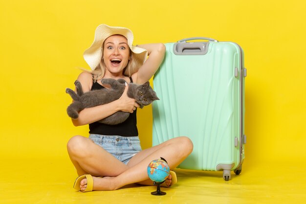 Вид спереди молодая женщина, сидящая со своей зеленой сумкой, держащая котенка на желтом столе, поездка, отпуск, путешествие, цвет моря, путешествие, солнце