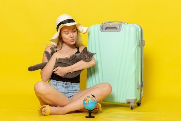 Вид спереди молодая женщина, сидящая со своей зеленой сумкой, держащая котенка на желтой стене, поездка, отпуск, путешествие, море, цвет, путешествие, солнце