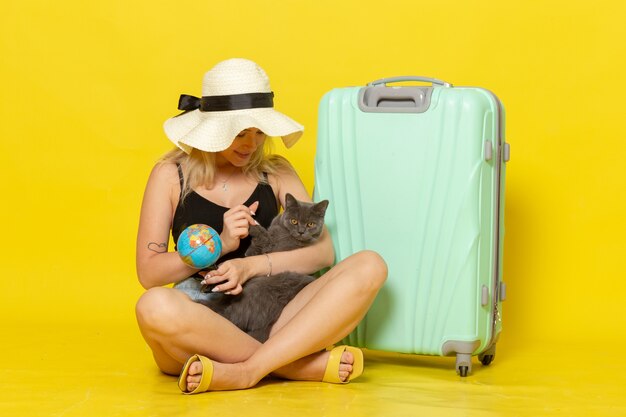 黄色の壁旅行休暇航海海の旅の太陽に子猫を抱き締める彼女の緑のバッグと一緒に座っている正面図若い女性