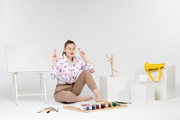 Front view young female sitting with paints and easel for drawing on a white background