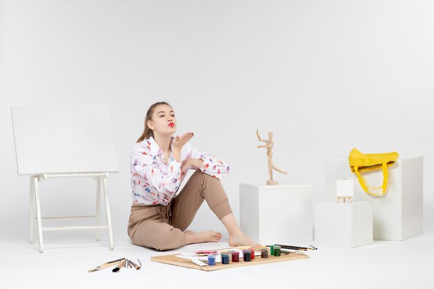 Front view young female sitting with paints and easel for drawing on a white background