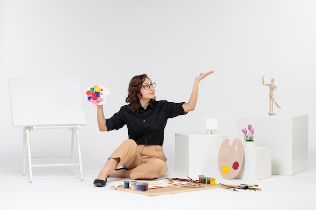 Front view young female sitting with paints and easel on a white background