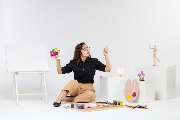 Free photo front view young female sitting with paints and easel on white background