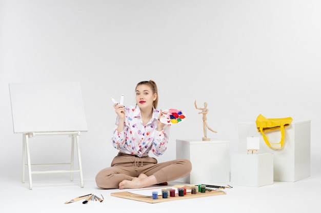 Front view young female sitting with paints and easel on white background