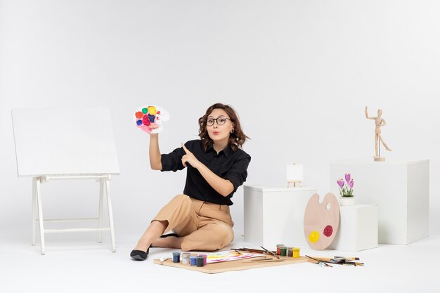 正面図白い床に絵の具とイーゼルで座っている若い女性カラー画家の描画アーティストアート女性の描画