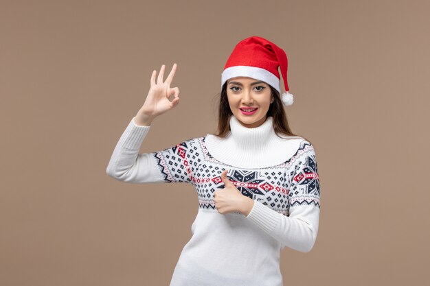 Front view young female smiling with red cap on brown background emotion christmas new year