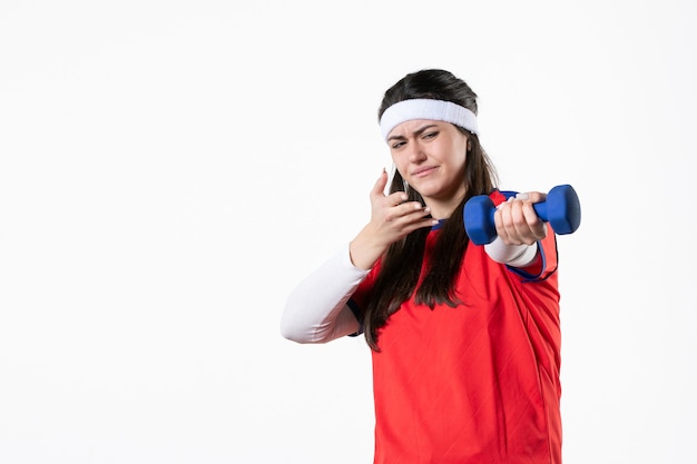 Front view young female in sport clothes with blue dumbbells on white wall