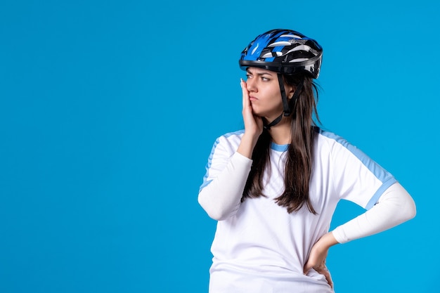 Вид спереди молодая женщина в спортивной одежде со шлемом на синей стене