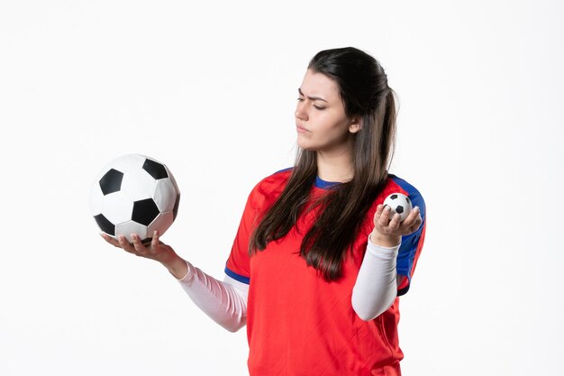 白い壁にサッカーボールとスポーツ服の若い女性の正面図