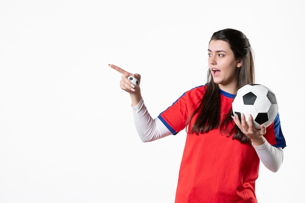白い壁にサッカーボールとスポーツ服の若い女性の正面図