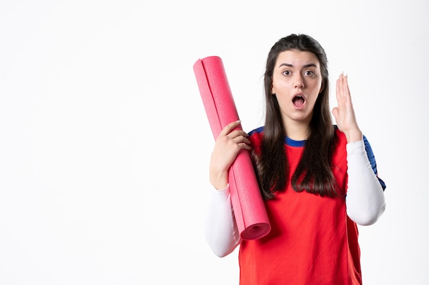 Giovane femmina di vista frontale in vestiti di sport con la parete bianca della stuoia di yoga