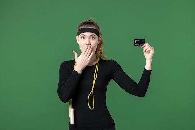 Front view young female in sport clothing holding bank card on green background workout body flex sport athlete woman money