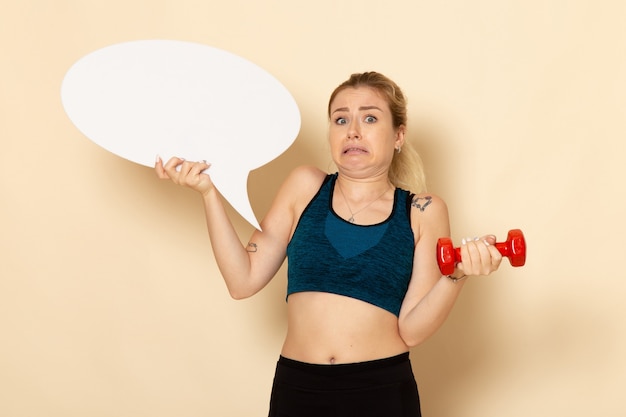 Free photo front view young female in sport outfit holding dumbbells and white speech bubble